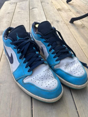 Nike Air Jordan 1 Low UNC blå/vit - Säljer ett par Nike Air Jordan 1 Low i färgen UNC blå och vit med svarta detaljer. De är slitna men funktionella