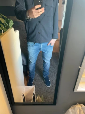 Ljusblå slim fit jeans från Replay - Säljer ett par ljusblå slim fit jeans från Replay med klassisk femficksmodell och snygga slitningar framtill. Jeansen har normal midja och raka ben, tillverkade i mjukt denimtyg som ger en skön passform. Perfekta för en avslappnad och trendig look.