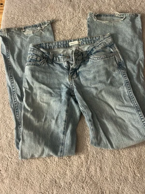 Ljusblå raka jeans från Levi's - Säljer ett par ljusblå jeans från Gina med rak passform och klassisk femficksdesign. Jeansen har slitna detaljer vid bensluten och bakfickor med lock och knapp.