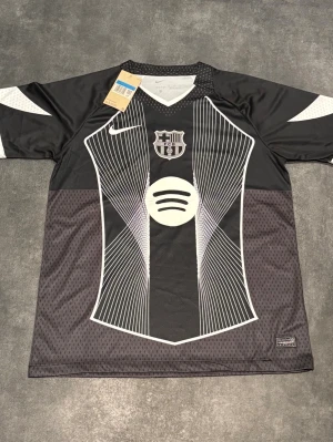 FC Barcelona fotbollströja Rashford Player edition - Snygg svart FC Barcelona matchtröja från Nike med vita grafiska linjer, klubbmärke och Spotify-logga på bröstet. På ryggen står det Rashford och nummer 14 i vitt. Tröjan har korta ärmar och är gjord i ett lätt, ventilerande material.