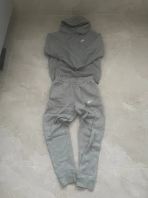 Grå Tracksuit från Nike - Säljer en grå tracksuit från Nike med klassisk logga broderad i vitt på benet och på tröjan. Storleken på tröjan är XS men skulle säga att den är närmare S, storleken på byxan är S. Skicket är mycket bra. Pris går att diskutera☺️