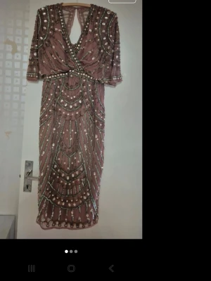 Rosa paljettklänning med öppen rygg - Unik rosa långklänning med paljetter och pärlor i ett glittrigt mönster. Klänningen har omlott framtill, trekvartsärm och en snygg öppen rygg. Perfekt för dig som vill sticka ut på festen!