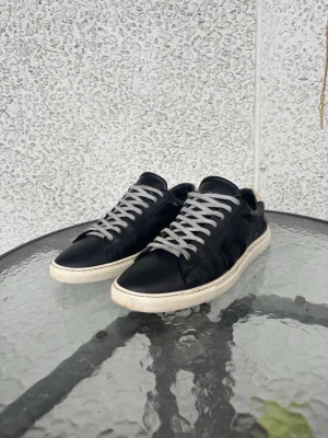 Svarta sneakers från Oliver Cabell - Stilrena svarta sneakers från Oliver Cabell i läder med vita sulor och gråa skosnören. Klassisk låg modell med rund tå och diskret logga på plösen. Perfekta för dig som gillar minimalistisk och clean stil. Säljes pågrund av att dem ej användes, jättefina skor som har mycket kvar att ge! Kom gärna med bud och är öppen för byten! Pris kan även diskuteras!