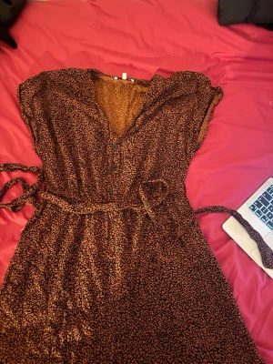 Brun leopardmönstrad jumpsuit med knappar - Säljer en brun jumpsuit  med leopardmönster och knappar framtill. Jumpsuit har v-ringning, knytband i midjan och är ärmlös. Perfekt för dig som gillar djurmönster och vill ha en avslappnad men snygg look.