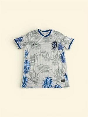 Nike Brasil fotbollströja☀️ - Snygg fotbollströja från Nike med Brasil-tryck och blått mönster av palmblad på vit botten. Tröjan har blå detaljer vid krage och ärmslut samt Nike-logga och Brasil-märke på bröstet. Perfekt för dig som vill sticka ut på planen.