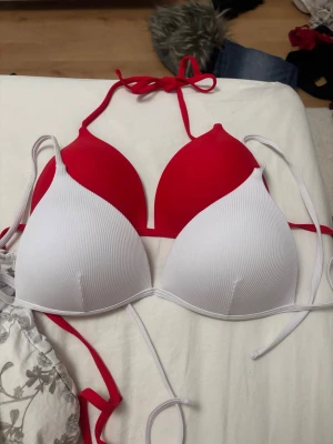 Bikiniöverdelar med push-up - Snygg röd och vit  bikiniöverdel med push-up och halterneck knytning i nacken. Enkel och stilren design utan mönster eller detaljer. Perfekt för strand eller poolhäng. Storleken är M och skulle säga att den passar C/D kupor. De är aldrig använda då jag inte gillar triangel bikini men hade jag gjort det så var de perfekta. Säljer båda två men om ni bara vill ha en så hör av er så löser vi det. 