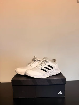 Vita Adidas sneakers med svarta ränder - Säljer ett par vita sneakers från Adidas med klassiska svarta ränder på sidan. Skorna har en sportig design med mesh- och syntetmaterial för bra andningsförmåga och komfort. Perfekta för träning eller vardagsstil. Snygga och lätta att matcha.