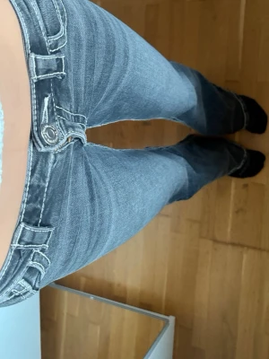 Gråa bootcut jeans med kontrastsömmar - Säljer ett par gråa bootcut jeans med tydliga kontrastsömmar och låg midja. Jeansen har klassisk femficksdesign och är tillverkade i ett stretchigt denimtyg som sitter snyggt på benen. Perfekta för en avslappnad och trendig look.