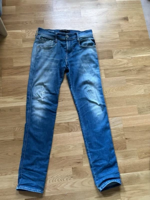 Blå Replay jeans med slitningar - Säljer ett par blå jeans från Replay med snygga slitningar och tvättade detaljer. Klassisk femficksmodell med normal midja och raka ben. Jeansen är gjorda i denim och har coola kontrastsömmar. Perfekta för en avslappnad och trendig stil.