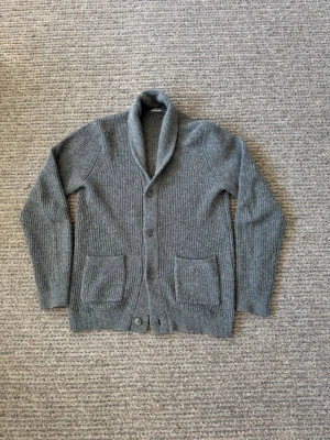 Cardigan - Mysig grå stickad kofta med sjalkrage och knäppning framtill. Två stora fickor framtill ger en chill vibe. Perfekt för lager på lager och passar till det mesta. Materialet känns mjukt och värmande, troligen ull eller ullmix.