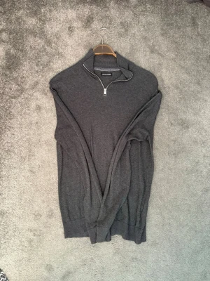 Mörkgrå halvzip-tröja Jack & Jones - Mörkgrå stickad tröja från Jack & Jones med halv dragkedja vid halsen. Tröjan har lång ärm och en klassisk, stilren look. Perfekt för lager på lager och enkel att matcha med olika outfits. Inte använd mycket