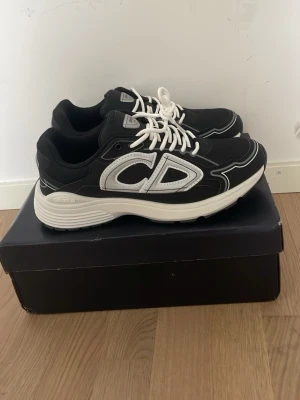 Svarta CD skor b30 - Snygga svarta sneakers från CD med vit tjock sula och vita detaljer. Skorna har stora CD-loggor på sidan och bak, samt vita skosnören. Materialet är en mix av textil och syntet, perfekt för en trendig streetwear-look. Helt nya kan mötas upp eller skicka bor u Vasastan