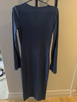 Mörkblå ribbad långklänning - Säljer en mörkblå ribbad långklänning med v-ringning och långa ärmar. Klänningen har en smal passform och är tillverkad i ett stretchigt material som sitter snyggt på kroppen. Perfekt för dig som gillar enkel men stilren design.