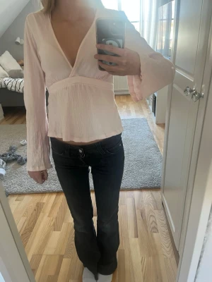 Ljusrosa omlottblus med knytband - Söt ljusrosa omlottblus med djup v-ringning och långa ärmar. Blusen har ett knytband i midjan som ger en fin siluett och är tillverkad i ett lätt, något skrynkligt tyg. Perfekt att styla med jeans eller kjol för en trendig look.