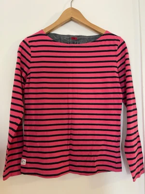 Randig långärmad topp i rosa och svart - Snygg långärmad topp med rosa och svarta horisontella ränder köpt i Stadium. Klassisk rak passform och rund halsringning. Tillverkad i mjuk bomull som känns skön mot huden. 