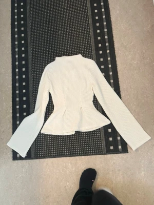 Vit ribbstickad peplumtröja - Säljer en vit ribbstickad tröja med peplumskärning och lång ärm. 