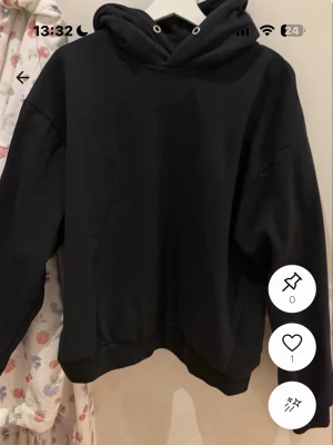 Svart basic hoodie med huva - En stilren svart hoodie med huva och dragsko. Modellen är enkel och oversized med ribbade muddar vid ärmslut och nederkant. Perfekt för en avslappnad och trendig look.