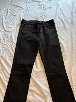 Svarta skinny jeans från Diesel - Säljer ett par svarta super slim-skinny jeans från Diesel, modell Skinzee-High med hög midja och stretchigt material. Klassisk femficksdesign och smal passform som sitter tajt hela vägen ner. Perfekta för dig som gillar en modern och stilren look.