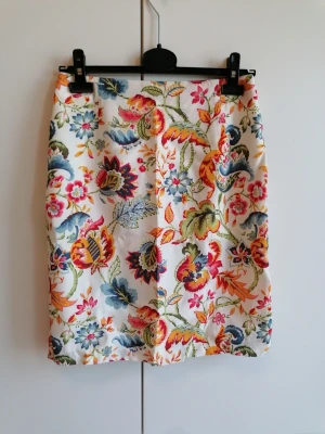 Blommig midikjol i viskos - Snygg vit kjol med färgglatt blommönster gjord i viskos. Rak modell som slutar vid knäna. Perfekt för dig som vill sticka ut med en färgsprakande look. Kjolen har en klassisk passform.