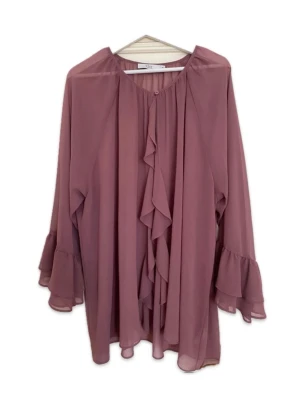 Volangblus med långa ärmar - Söt blus i dammig rosa ton med volangdetaljer framtill och vid ärmsluten. Tillverkad i ett tunt, transparent tyg som ger ett luftigt intryck. Rund halsringning och avslappnad passform. Perfekt för dig som gillar romantisk och trendig stil.