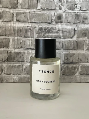ESSNCE Cozy Goddess Eau de Parfum - En stilren parfymflaska från Essnce med doften Cozy Goddess. Flaskan är cylindrisk i genomskinligt glas med svart lock och vit etikett med minimalistisk design. Perfekt för dig som gillar enkla och snygga detaljer på parfymhyllan. Endast test sprayad. 
