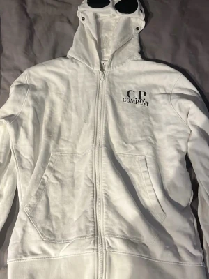  C.P. Company hoodie vit ÄKTA  - Säljer en vit hoodie från C.P. Company med dragkedja och ikoniska glasögon i huvan.  den står m men den passar mer  s den har inga skador eller något sånt öppen för byten och prisförslag  den är ökta och chippen finns kvar på tröjan 