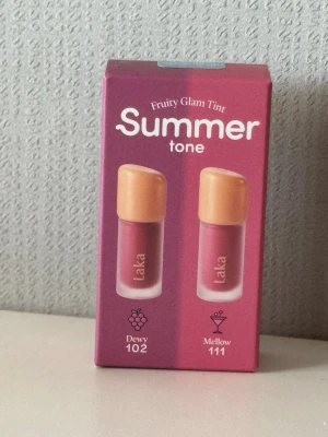 Laka Fruity Glam Tint Summer Duo - Laka Fruity Glam Tint Summer tone är ett läppglans-duo med två nyanser: Dewy 102, en bärig rosa, och Mellow 111, en mjukare rosa. Kommer i en snygg förpackning med guldiga lock. Perfekt för dig som gillar fräscha och somriga färger på läpparna.