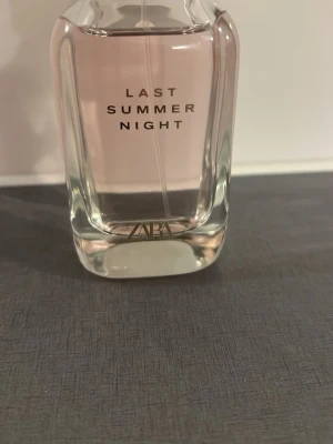 ZARA Last Summer Night parfym - En stilren parfymflaska från ZARA med doften Last Summer Night. Flaskan är transparent med mjukt rosa vätska och har en modern, kantig form. Texten är tryckt i vitt och flaskan är tillverkad i glas.