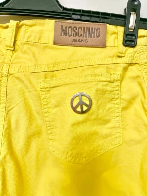 Gula Moschino-jeans  - Coola och iögonfallande jeans i en klargul “Lemon Yellow”-nyans från det ikoniska italienska lyxmärket Moschino, känt för sina färgstarka och lekfulla designer. Ett statement-plagg som verkligen sticker ut och lyfter vilken outfit som helst – perfekt för dig som gillar mode med personlighet och att våga synas.