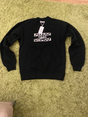 Svart sweatshirt från Vailent - Svart sweatshirt från Vailent med trycket 'Quiet CHAOS' på bröstet. Tröjan har rund halsringning, långa ärmar och ribbade muddar. Perfekt för en avslappnad och trendig stil.