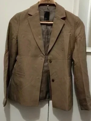 YK038 - Stilren beige kavaj från YK038,Korean brand med klassisk krage och två knappar framtill. Kavajen har två fickor och är helfodrad. Perfekt för en snygg och enkel look. Materialet är bomullsmix som ger en mjuk känsla.