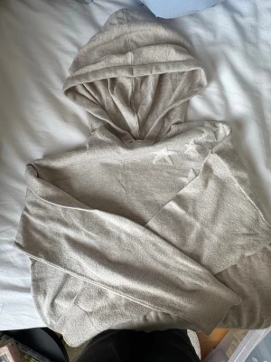 Beige hoodie från Gina Tricot - Mysig beige hoodie från Gina Tricot med huva och diskreta stjärndetaljer på axeln. Perfekt för en avslappnad stil och enkel att matcha med jeans eller leggings. Mjuk bomullskänsla och klassisk passform.