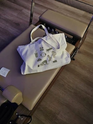 Helt ny Vit tygkasse reformer pilates - En rymlig och slitstark tygväska perfekt för pilates, refromer, yoga och annan träning- men lika användbar till vardag och shopping   Rymmer alt du behöver, från vattenflaska och träningskläder till dina daily essentials. Tillverkad i kraftigt material med förstärkt botten och starka sömmar som klarar upp till 25 kg Stilren design med pilates-inspirerade detaljer.   Specifikationer 45 x 35 x 8 cm Polyester/bomull Klarar upp till 25 kg Kan bäras i hand eller över axeln Aldrig använd 