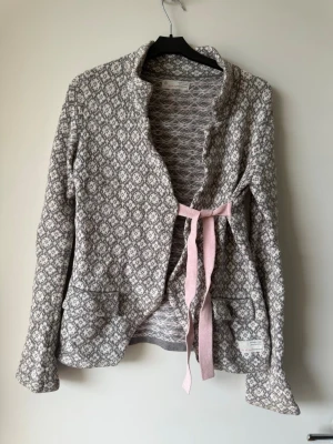 Mönstrad kofta från Odd Molly - Supersöt kofta från Odd Molly i grått och vitt med diskret mönster och rosa knytband framtill. Koftan har två fickor och en mjuk, skön känsla. Perfekt för lager-på-lager och ger en chill men ändå snygg look.