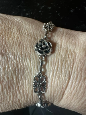 Silverfärgat armband med blommor - Ett stilrent armband i silverfärgad metall med detaljerade blommotiv och länkar. Armbandet har både öppna och fyllda blomdelar som ger en cool och unik look. Perfekt accessoar för dig som gillar boho eller vintage-inspirerad stil.