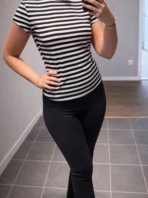 Svartvit randig t-shirt - Snygg svartvit randig t-shirt med korta ärmar och rund halsringning. T-shirten har en figurnära passform och är perfekt för en stilren och enkel look. Tillverkad i mjukt material som känns skönt mot huden.