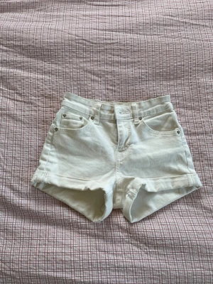 Vita högmidjade jeansshorts - Snygga vita jeansshorts med hög midja och klassisk femficksdesign. Shortsen har uppvikta benslut och bälteshällor, perfekta för en fräsch sommarlook. Passar till allt och är lätta att matcha med olika toppar. Från Bershka och är i storlek 32