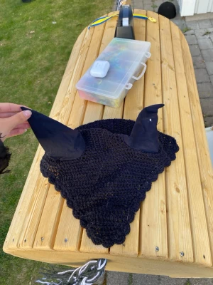 Svart virkad huva till häst - Svart virkad huva för häst med två spetsiga öron i tyg. Perfekt för att skydda hästens öron mot insekter eller dämpa ljud. Huvan har en klassisk trekantig form och är gjord i mjukt, luftigt material. Pris kan diskuteras. Storlek häst 