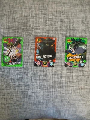 Teenage Mutant Ninja Turtles samlarkort - Tre samlarkort från Teenage Mutant Ninja Turtles-serien: Raph's Sai, The Rat King och Leatherhead. Färgglada kort med motiv av karaktärer och vapen, med gröna och röda ramar samt poäng och symboler. Perfekt för dig som gillar TMNT och samlarkort.