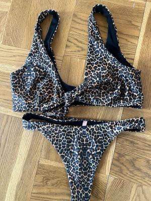 Leopardmönstrad bikini från Nelly - Snygg bikini med leopardmönster i brunt och svart. Man knyter överdelen framtill. Trosorna har storlek S och toppen har M. 