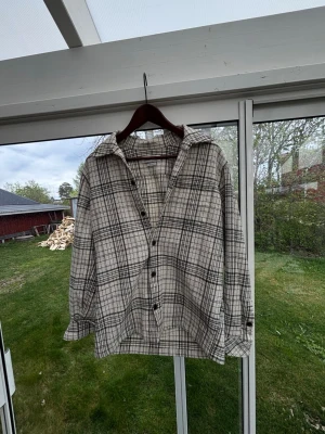 Rutig skjorta från Samsøe Samsøe - Snygg rutig skjorta från Samsøe Samsøe i beige och svart. Skjortan har klassisk krage, knappar framtill och långa ärmar. Tillverkad i ett lite grövre tyg som ger en cool och avslappnad look.