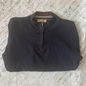 Mörkblå halvzip-tröja  - Snygg mörkblå långärmad tröja med halvzip och ribbade muddar. Klassisk ståkrage med randigt band på insidan och diskret broderad logga på bröstet. Perfekt för dig som gillar stilrena och tidlösa plagg. Storlek L men passar M