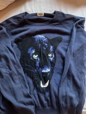 Mörkblå Weekday tröja med pantermotiv - Cool mörkblå tröja från Weekday med ett stort, detaljerat pantermotiv framtill. Tröjan har rund halsringning och ribbade muddar vid ärmslut och nederkant. Perfekt för dig som vill sticka ut med en unik design.