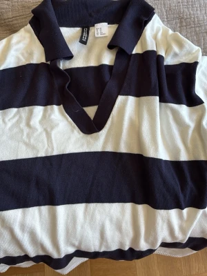 Randig tröja i stl Xs - Säljer en oversized pikéskjorta från Hm med breda marinblå och vita ränder. Skjortan har krage och v-ringad öppning utan knappare vilket ger en avslappnad look. Tillverkad i mjuk bomull, perfekt för en chill och sportig stil.