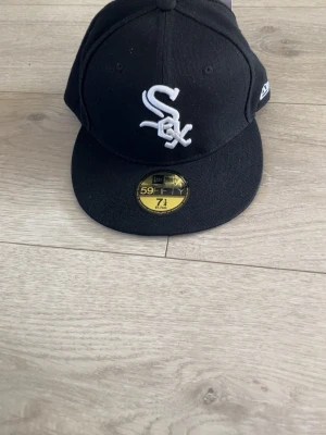 Svart White Sox keps från New Era - Snygg svart keps från New Era med White Sox-logga broderad i vitt framtill. Klassisk 59FIFTY-modell med platt skärm och MLB-logga baktill. Perfekt för dig som gillar streetwear och sportiga accessoarer.