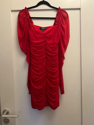 Röd draperad klänning från Missguided - Snygg röd klänning från Missguided med draperad design och puffiga ärmar. Klänningen har en tight passform och är tillverkad i ett stretchigt material som ger en cool och trendig look. Perfekt för dig som vill sticka ut med färg och form.