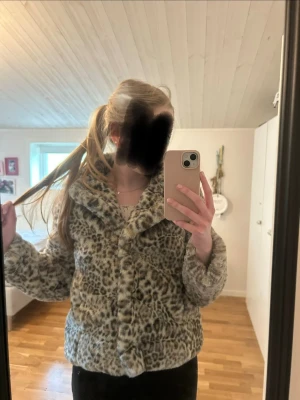 Leopardmönstrad pälsjacka - Säljer en fluffig och trendig leopardmönstrad pälsjacka i beige och grå toner. Jackan har bred krage, knäppning framtill och är gjord i fuskpäls som ger en lyxig känsla. Perfekt för dig som vill sticka ut och hålla dig varm under vintern.