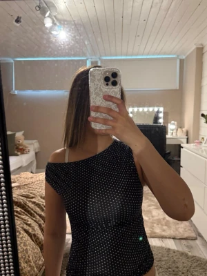 Svart prickig oneshoulder topp - Snygg svart oneshoulder topp med vita prickar. Toppen har en tight passform och ärmlös design. Obs: kommer från Shein. Säljs pga: lite tajt i armarna