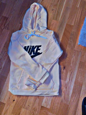 Beige hoodie från Nike med logga - Säljer en beige hoodie från Nike med stor svart logga på bröstet. Hoodien har huva med snörning och ribbade muddar vid ärmslut och nederkant. Perfekt för dig som gillar sportig och avslappnad stil. Tjej passar xs / smal  dressen ;@; 500