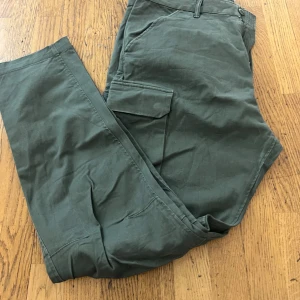 Mörkgröna cargopants med raka ben - Snygga mörkgröna cargopants med raka ben och stora fickor på sidorna. Byxorna har klassisk cargostil med bälteshällor och är tillverkade i ett slitstarkt bomullstyg. Perfekta för en avslappnad och trendig look.